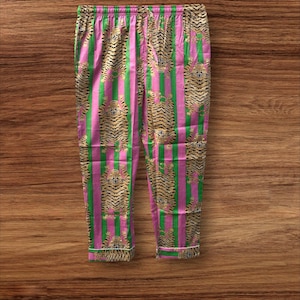 May include: Pink and green striped pajama pants with a tiger print. The pants have a drawstring waist and white trim at the cuffs. The tiger print is in shades of brown and black.