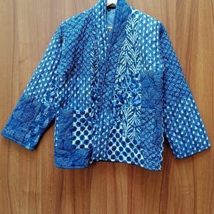 Könnte beinhalten: Eine blaue gesteppte Jacke mit Patchwork-Design, das verschiedene Muster aus Kreisen, Punkten und Linien zeigt. Die Jacke hat lange Ärmel und einen Kragen.