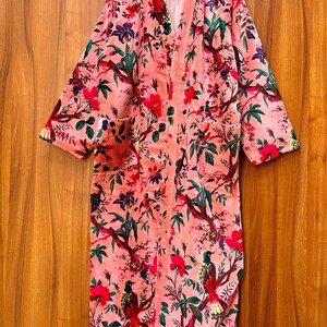 Peut inclure: Une robe de chambre rose &agrave; imprim&eacute; floral avec des manches longues et une ceinture &agrave; nouer. La robe pr&eacute;sente un motif floral avec des oiseaux et des feuilles.