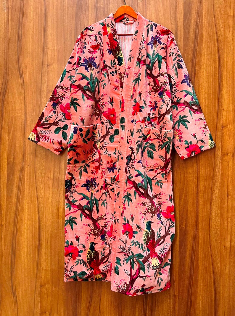 Peut inclure: Une robe de chambre rose &agrave; imprim&eacute; floral avec des manches longues et une ceinture &agrave; nouer. La robe pr&eacute;sente un motif floral avec des oiseaux et des feuilles.