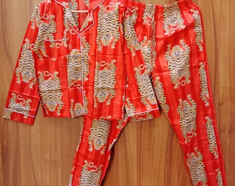 Op de afbeelding: Rode pyjamaset met tijgerprint. De set bevat een overhemd met knopen, witte bies en een bijpassende broek. Het tijgerpatroon is in bruin- en zwarttinten op een rode gestreepte achtergrond.