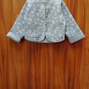 May include: A gray quilted jacket with a white floral pattern and a button closure. The jacket has two pockets and striped cuffs.