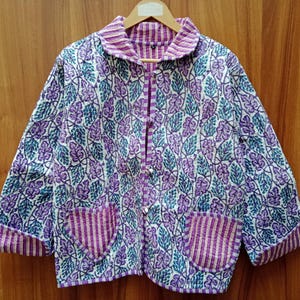 May include: A purple and blue floral patterned jacket with a white background. The jacket has a collar, long sleeves, and two pockets. The jacket is made of a soft, quilted fabric.
