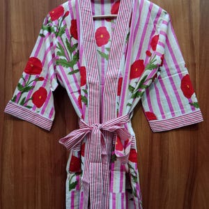 May include: A pink and white striped robe with red poppy floral embroidery. The robe has a self-tie sash and long sleeves.