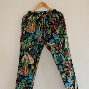May include: Black pajama pants with a vibrant floral and figure print. The pants feature a drawstring waist and a colorful design with red, green, and blue elements. The fabric is patterned with tropical foliage and figures.