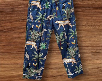 May include: Blue pajama pants with a jungle-themed print featuring leopards, zebras, toucans, and palm trees. The pants have a drawstring waist and white trim along the cuffs and pockets. The fabric has a soft, comfortable appearance.