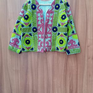 May include: A green, pink, and blue embroidered jacket with a geometric pattern. The jacket has a zipper closure and long sleeves.
