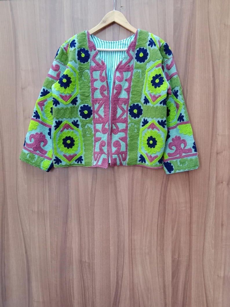 May include: A green, pink, and blue embroidered jacket with a geometric pattern. The jacket has a zipper closure and long sleeves.