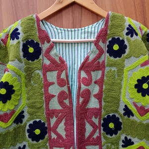 May include: A green, red, and blue embroidered jacket with a floral pattern. The jacket has a V-neck and is open in the front.