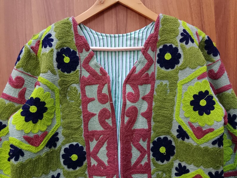 May include: A green, red, and blue embroidered jacket with a floral pattern. The jacket has a V-neck and is open in the front.