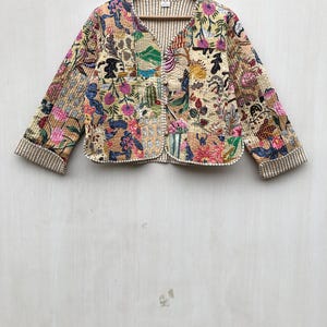 Pode incluir: Uma jaqueta acolchoada de cor creme com estampa floral. A jaqueta tem fecho de botão e mangas compridas. As mangas têm um padrão listrado.