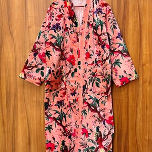 Peut inclure: Une robe en velours rose avec un imprim&eacute; floral et d'oiseaux. La robe a une silhouette longue et fluide et une fermeture &agrave; nouer &agrave; l'avant.