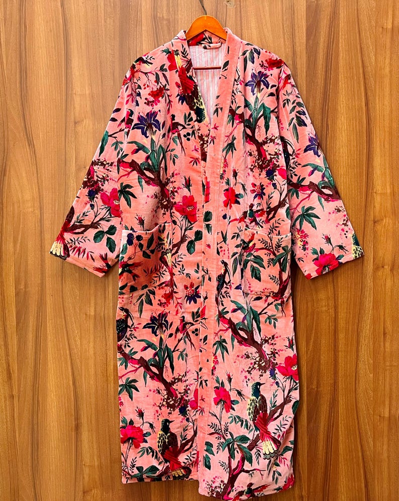 Peut inclure: Une robe en velours rose avec un imprim&eacute; floral et d'oiseaux. La robe a une silhouette longue et fluide et une fermeture &agrave; nouer &agrave; l'avant.