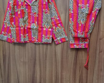 Peut inclure: Un ensemble pyjama rayé rouge et orange avec un imprimé tigre. Le haut a un devant boutonné et des manches longues. Le pantalon a une taille élastique.