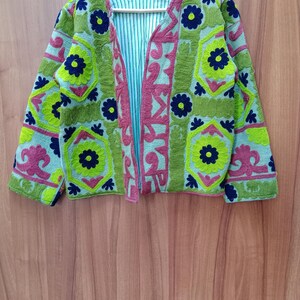 May include: A green, blue, and pink embroidered jacket with floral patterns. The jacket has a V-neck and long sleeves.