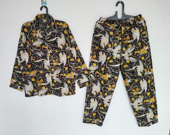 Peut inclure: Ensemble de pyjama noir avec un motif d'oiseaux blancs et de fruits jaunes. Le haut à manches longues a une fermeture boutonnée et une bordure blanche. Le pantalon assorti a une taille élastique. L'ensemble est en matière douce et confortable.