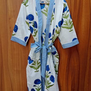 Könnte beinhalten: Weißer Baumwoll-Bademantel mit blauem Blumendruck und blau-weißem Streifenbesatz. Der Bademantel hat einen Bindegürtel und Dreiviertelärmel.