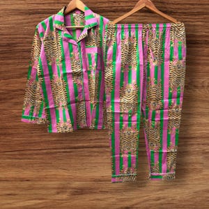 Op de afbeelding: Een tweedelige pyjamaset met roze en groene strepen en een tijgerprint. De top met lange mouwen heeft een knoopsluiting en een borstzak. De broek heeft een elastische tailleband. De set wordt gepresenteerd op een houten hanger. Afmetingen in centimeters.