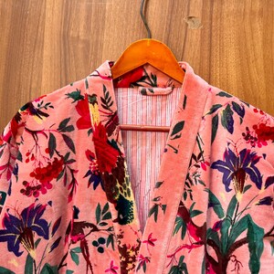 Peut inclure: Une robe en velours rose avec un imprim&eacute; floral repr&eacute;sentant des oiseaux, des fleurs et des feuilles. La robe a un col en V et une fermeture &agrave; nouer.