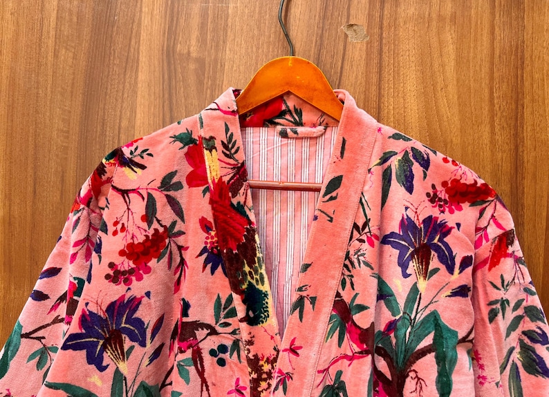 Peut inclure: Une robe en velours rose avec un imprim&eacute; floral repr&eacute;sentant des oiseaux, des fleurs et des feuilles. La robe a un col en V et une fermeture &agrave; nouer.