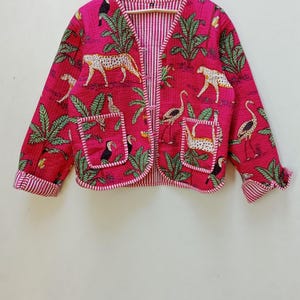 May include: A pink quilted jacket with a green and white tropical print featuring toucans, leopards, and flamingos. The jacket has a button closure and two pockets.