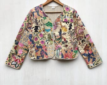 May include: A beige quilted jacket with a V-neck, adorned with a patchwork of floral and abstract designs in pink, blue, and green. The jacket, hanging on a wooden hanger, displays an open front and intricate stitching details, showcasing its unique style.
