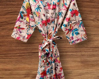 May include: A beige floral print robe with a colorful bird and flower pattern. The robe has a tie closure and white trim. The robe is hanging on a wooden hanger against a wooden background.