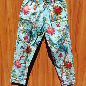 Può includere: Un paio di pantaloni blu chiaro con stampa floreale. I pantaloni hanno una cintura elastica e un cordoncino.