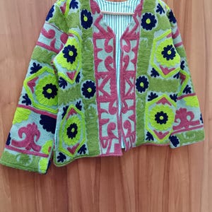 May include: A green, pink, and blue embroidered jacket with floral patterns. The jacket has a V-neck and long sleeves.
