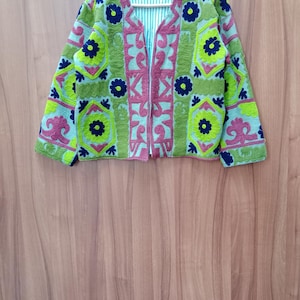 May include: A green, pink, and blue embroidered jacket with a floral pattern. The jacket has a zipper closure and long sleeves.