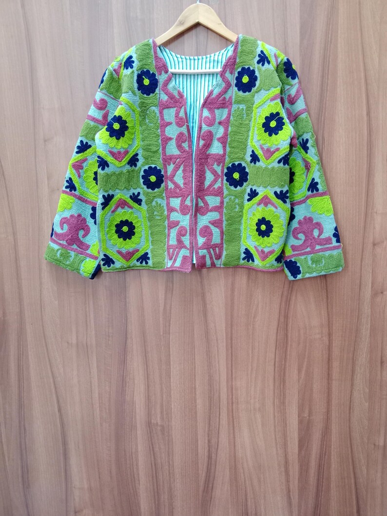 May include: A green, pink, and blue embroidered jacket with a floral pattern. The jacket has a zipper closure and long sleeves.