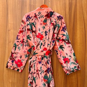 Peut inclure: Une robe en velours rose avec un imprim&eacute; floral et d'oiseaux. La robe a une ceinture &agrave; nouer et des manches longues.