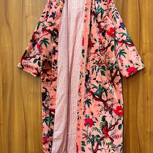 Peut inclure: Une longue robe de chambre rose &agrave; imprim&eacute; floral avec une doublure ray&eacute;e. La robe a un col large et des manches longues.