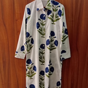 May include: White long-sleeve shirt dress with a blue floral pattern. The dress features a button-down front, a collared neckline, and a knee-length hem. The floral design includes blue flowers and green leaves.