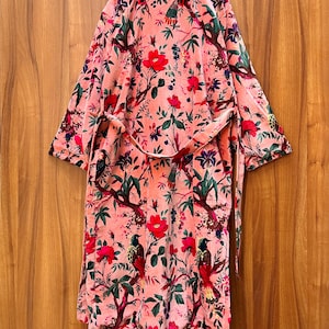Peut inclure: Une robe en velours rose avec un imprim&eacute; floral et d'oiseaux. La robe a une ceinture &agrave; nouer et des manches longues.