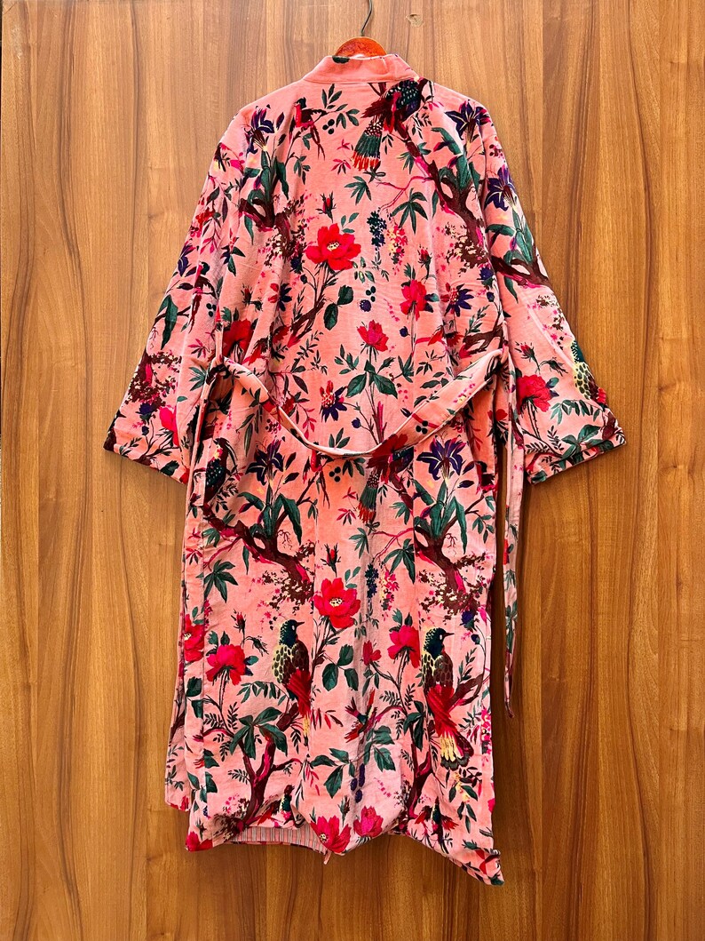 Peut inclure: Une robe en velours rose avec un imprim&eacute; floral et d'oiseaux. La robe a une ceinture &agrave; nouer et des manches longues.