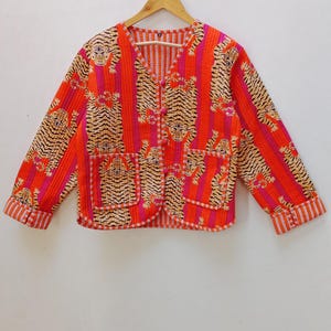 Może przedstawiać: Kurtka pikowana w kolorze czerwonym i różowym z nadrukiem tygrysa i zapięciem na guziki. Kurtka ma dekolt w kształcie litery V i długie rękawy.