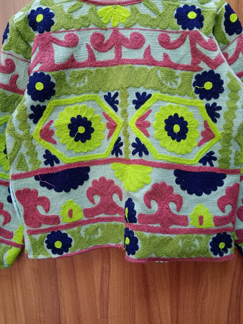 May include: A green, pink, and blue embroidered jacket with floral and geometric patterns.
