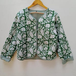 Op de afbeelding: Een groen en wit gewatteerd jack met een bloemen- en vogelprint. Het jack heeft een V-hals en een knoopsluiting.