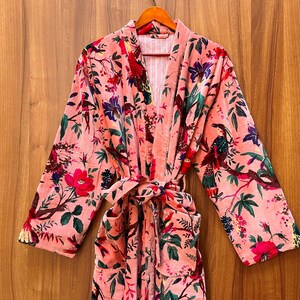 Peut inclure: Une robe en velours rose avec un imprim&eacute; floral repr&eacute;sentant des oiseaux et des fleurs. La robe a une ceinture &agrave; nouer et deux poches.