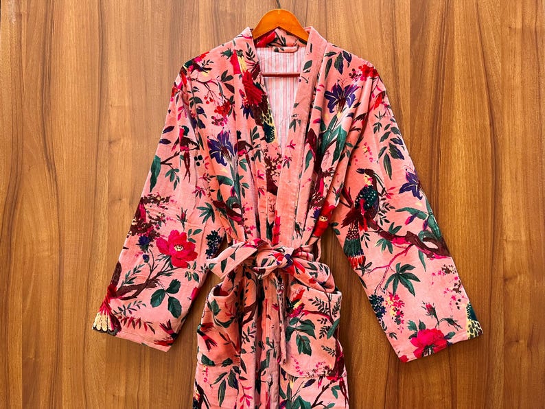 Peut inclure: Une robe en velours rose avec un imprim&eacute; floral repr&eacute;sentant des oiseaux et des fleurs. La robe a une ceinture &agrave; nouer et deux poches.