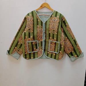 以下が含まれることがあります： 緑と茶色のキルティングジャケットで、虎柄と緑のストライプが入っています。ジャケットはVネックでボタン留めです。袖は白と青のストライプのトリムになっています。