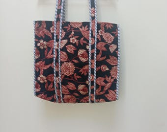 May include: Black tote bag with a floral print in shades of red and white. The bag has white and blue striped trim around the edges.