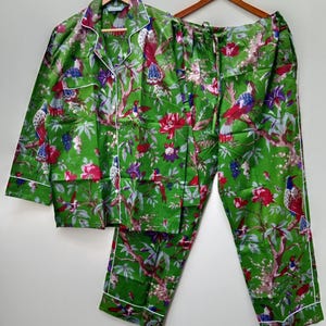 May include: Green pajama set with a vibrant floral and bird print. The long-sleeved top has white piping and buttons, and the pants have a drawstring waist. The set is made of a soft, lightweight fabric.