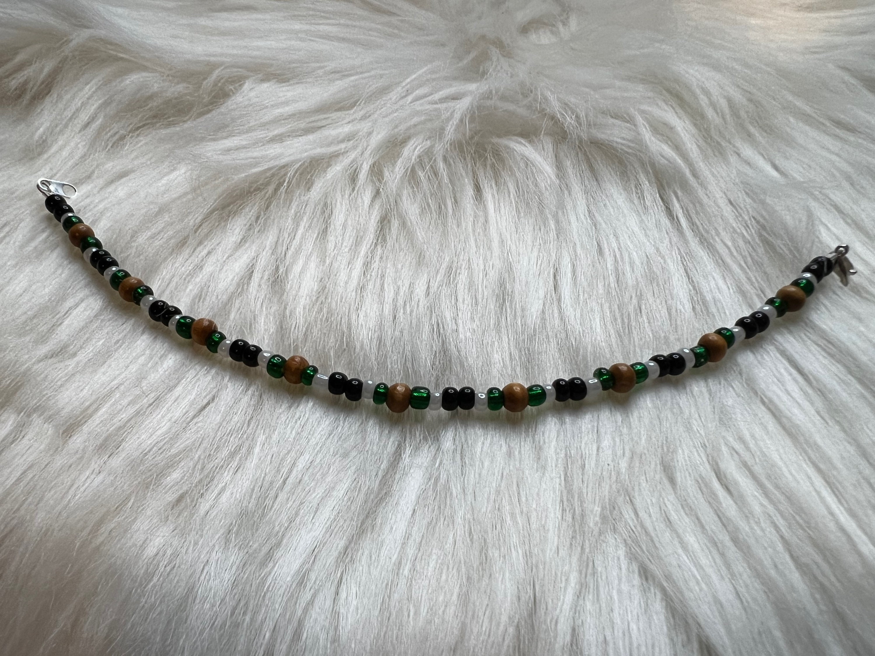 Beaded Bracelet in Black Tan and Greens on a Matte Bronze Background. Browns