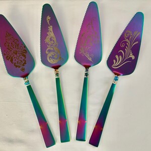 May include: Four iridescent cake servers with gold-coloured designs. The servers have a purple, blue, and green iridescent finish.