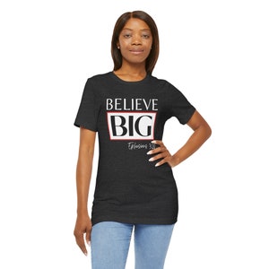 Könnte beinhalten: Ein dunkel-melierter grauer T-Shirt mit einer weißen Grafik, auf der "BELIEVE BIG" in einem roten Kasten steht. Der Text "Ephesians 3:20" ist in weiß unter dem Kasten geschrieben.