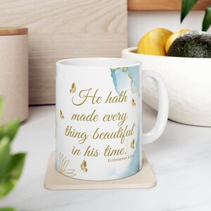 May include: White ceramic mug with a blue and gold watercolor design. The mug features the quote "He hath made every thing beautiful in his time." with the scripture reference "Ecclesiastes 3:11" in gold lettering.
