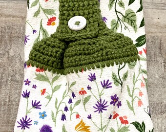 Armário suspenso para cozinha com topo em crochê e fechamento por botões, estampa de flores silvestres em tons de coral, verde-sálvia, violeta e azul sobre fundo branco.