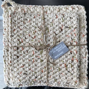 Peut inclure: Ensemble de deux torchons et maniques en crochet de couleur beige avec des accents verts et orange. L'ensemble est relié par une ficelle et une étiquette qui indique "Set-Matching Pot Holders & Dish Cloth Handmade".